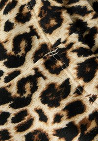 Nærbilde av mykt stoff med leopardmønster i beige, brune og svarte toner, med synlige søm detaljer.