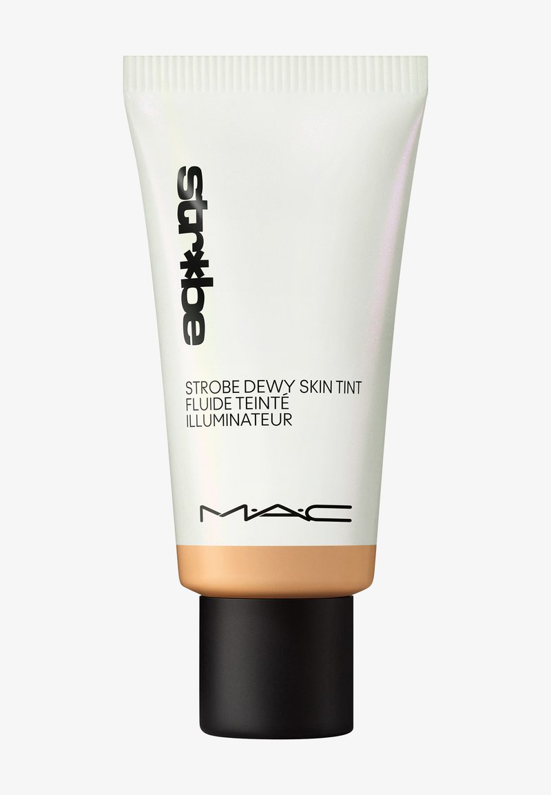 MAC Strobe Dewy Skin Tint dans un tube blanc avec des lettres noires, une base bronzée et un capuchon noir. Texture lisse, design minimaliste.