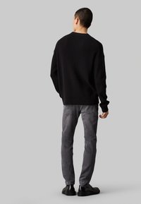 Maglione nero a costine, vestibilità rilassata, scollatura rotonda. Abbinato a jeans in denim grigi e stivali neri con lacci. Visualizzato da dietro.