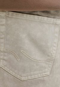 Tissu beige à texture côtelée, avec une poche arrière à coutures beiges et un design subtil incurvé. Aucun élément métallique ni motif visible.