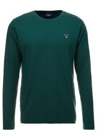 Dunkelgrünes langärmeliges Crewneck-Shirt mit kleinem GANT-Logo auf der linken Brust, auf weißem Hintergrund dargestellt.