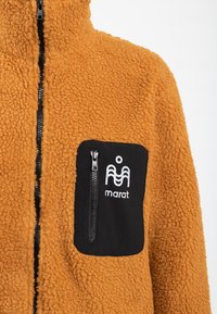 Pomarańczowa polarowa kurtka o textured powierzchni, z przednim zamkiem błyskawicznym i czarną kieszenią na zamek z logo oraz białym brandingiem.