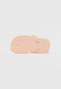 Sola de sapato rosa-claro com uma textura estriada. Duas depressões circulares e seções suaves são visíveis, indicando um design minimalista.