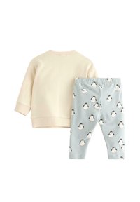 Helle beige Sweatshirt mit langen Ärmeln, kombiniert mit hellblauen Leggings, die ein Pinguin-Muster in Schwarz, Weiß und Orange aufweisen.