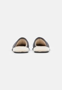 A szürkés slip-on papucsok puha, bolyhos fehér béléssel, texturált felsőrésszel és lapos fekete talppal rendelkeznek. A dizájn hátul nyitott.
