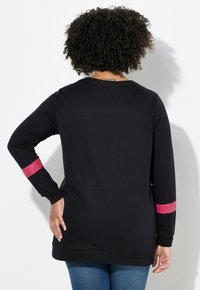 Maglietta nera a maniche lunghe con dettagli in glitter rosa sulle maniche. Presenta un collo rotondo e tasche laterali, realizzata in un materiale morbido e elasticizzato.