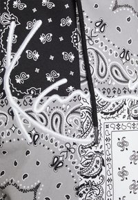 Černobílá tkanina s bandana vzorem a paisley designy, obsahující texturované akcenty a výrazné bílé vyšívané logo.