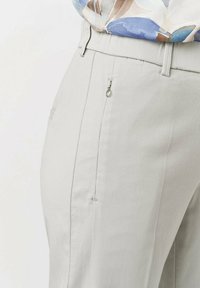 Hellgraue Hose aus strukturiertem Stoff mit einer Seitentasche und einem silbernen Reißverschlussdetail sowie einem glatten Taillendesign.