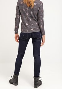 Mörkgrå långärmad tröja med stjärnmönster, kombinerad med tajta mörkblå jeans och svarta ankelboots. Fokusera på avslappnad stil.