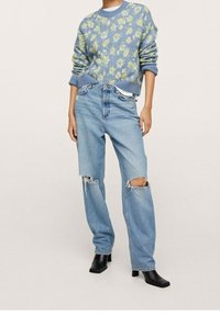 Hellblauer Pullover mit Blumenmuster und gerippten Bündchen; hellblaue Jeans mit großen Knierissen; schwarze Stiefeletten mit Blockabsatz.