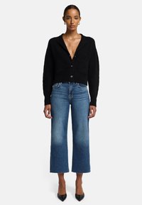 Cardigan nero corto con scollo a V, due tasche frontali e chiusura a bottoni, abbinato a jeans a gamba larga azzurri e décolleté nere a punta.