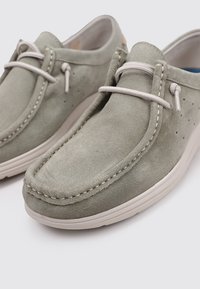 Zapatos sin cordones de ante gris con puntera redondeada, costuras claras en contraste y suela de goma flexible. Presentan cordones decorativos y agujeros de ventilación.