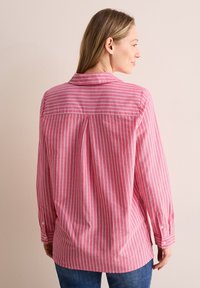 Camicia a maniche lunghe a righe rosse e bianche con piega sul retro, polsini con bottone e colletto classico. Il tessuto appare leggero e traspirante.