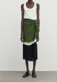 Groene wikkelrok met een verloopontwerp met witte en zwarte accenten, gecombineerd met een wit tanktop en zwarte sandalen. Glad textuur.