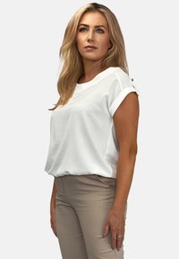 Biała krótka bluzka z luźnym krojem, z podwiniętymi mankietami i subtelną teksturą; zestawiona z jasnobeżowymi dopasowanymi spodniami.