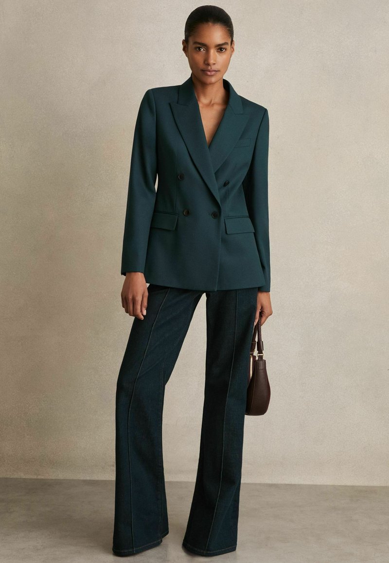 Zilgan dubultajām jostām ar kātiem, saskaņoti ar tumši izplestām džinsu biksēm. Pievēršiet uzmanību pulētajām detaļām un strukturēto piegriezumu.