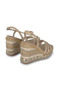 Sandali wedge beige con cinturini incrociati, piattaforma intrecciata testurizzata, dettagli metallici e gemme trasparenti lungo la suola.
