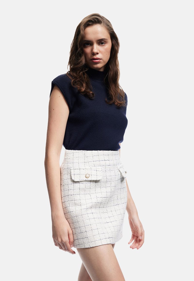 Top de manga corta en color marino con un cuello alto, combinado con una falda blanca con textura de cuadros que cuenta con dos bolsillos frontales y detalles de botones.