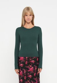 Grønneribbet langærmet bluse med rund halsudskæring, parret med en blomsterprintet sort nederdel med pink, rød og grønne mønstre.