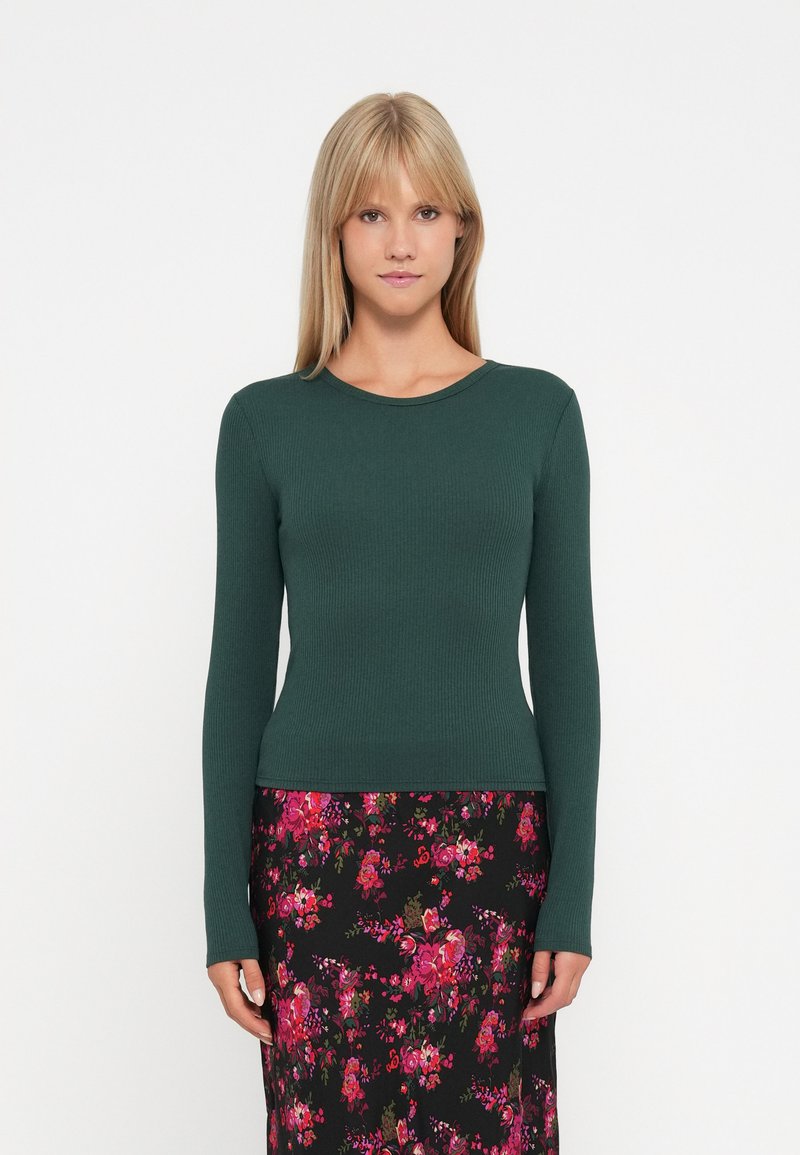 Grønneribbet langærmet bluse med rund halsudskæring, parret med en blomsterprintet sort nederdel med pink, rød og grønne mønstre.