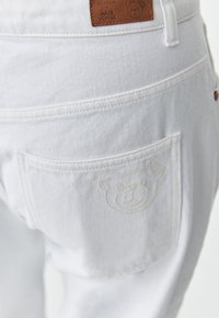Jeans in denim bianco con finitura testurizzata, una tasca posteriore con logo dell'orso in rilievo e un'etichetta in pelle marrone sulla vita.