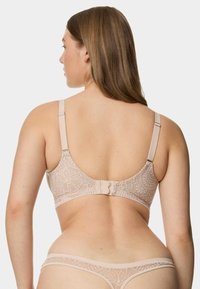 Reggiseno in pizzo beige con motivo floreale e spalline regolabili. Presenta una chiusura a gancio e occhiello e un perizoma in pizzo abbinato. Texture liscia.