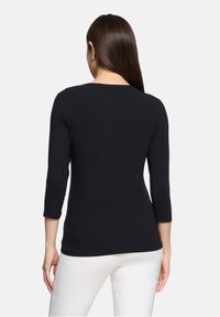 Czarny top z rękawami 3/4 wykonany z miękkiego materiału, z okrągłym dekoltem i dopasowanym krojem. Połączony z białymi spodniami.