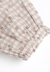 Tissu à motifs rose et beige avec un design en grille et de petits accents floraux ; présente un poignet froncé avec une finition texturée.