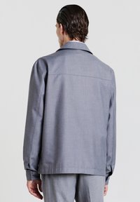 Giacca grigia con un fit rilassato, maniche lunghe, ampio colletto e dettaglio sullo yoke posteriore. Realizzata in tessuto testurizzato.