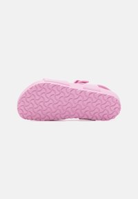 Pink footwear with a textured rubber sole. The upper features wide straps and a secure closure, designed for comfort and easy wear.