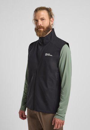 Schwarze ärmellose Weste mit hohem Kragen, ausgestattet mit einem Reißverschluss vorne und einem Logo auf der Brust. Getragen über einem grünen Langarmshirt.