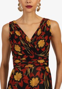 Blumenkleid mit V-Ausschnitt, das rote, gelbe und grüne Muster auf einem schwarzen Hintergrund zeigt. Strukturierte Faltenlegung am Oberteil.
