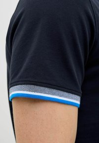 Zwarte polo met een gestructureerde stof, voorzien van een blauw-wit gestreepte accent bij de kraag en de mouwranden.