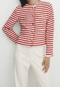 Veste rayée rouge et blanche à manches longues, col rond, avec des boutons dorés sur le devant. Tissu texturé avec une coupe ajustée.