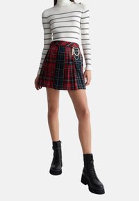 Sort og rød ternet plisseret nederdel med kæde detaljer, parret med en hvidstribet rullekrave og sorte ankelstøvler.