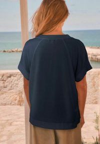 Marinblå kortärmad topp med avslappnad passform, med rund halsringning och uppvikta ärmar, tillverkad av lätt tyg. Enkel design, utan mönster.
