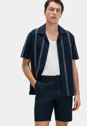 Camisa de manga corta azul marino con rayas blancas, diseño abotonado, combinada con pantalones cortos azul marino. Tejido ligero y texturizado, ajuste casual.