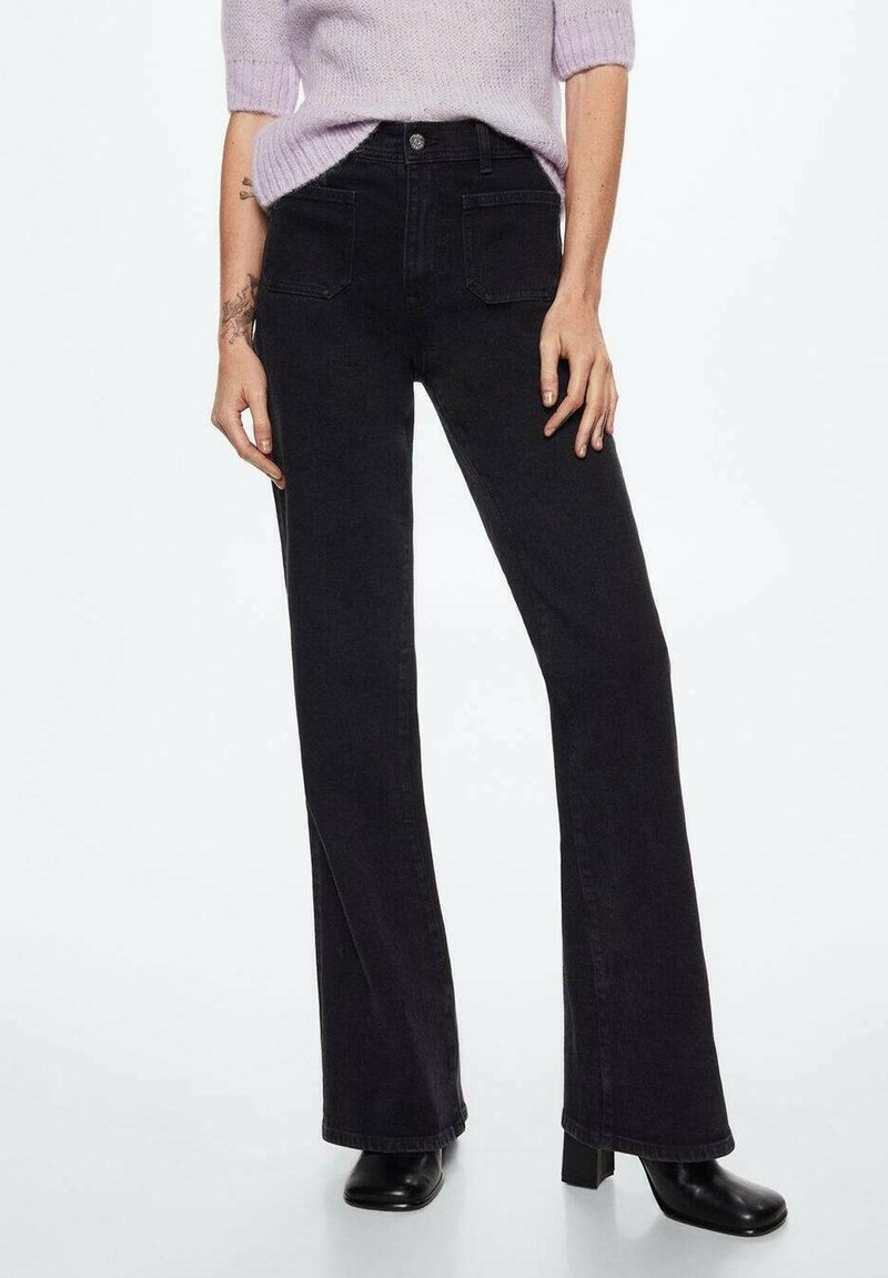 Personne portant un jean noir taille haute à jambes larges, associé à des bottes à talons noires et un pull lavande à manches courtes rentré dans le pantalon.