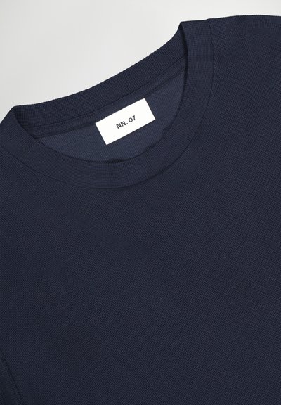 Marineblaues, strukturiertes Langarmshirt mit Rundhalsausschnitt und einem weißen Etikett, das innen am Kragen mit "NN. 07." eingenäht ist.