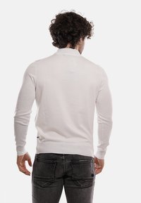 Maglione bianco a maniche lunghe con design attillato, polsini e scollatura a coste; texture leggera e liscia, abbinato a jeans scuri.