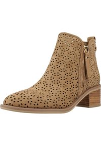 Botín beige hasta el tobillo hecho de ante perforado, con puntera redonda y tacón bajo apilado. Cuenta con un zipper lateral para un fácil acceso.