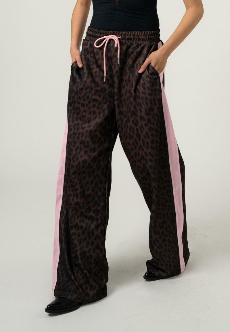 Pantaloni a vestibilità ampia con stampa leopardata scura, strisce laterali rosa, vita con coulisse rosa, indossati con un top nero e scarpe nere.