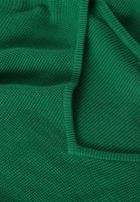 Tissu tricoté vert, présentant un motif texturé, avec un bord lisse. Le matériau semble doux et flexible, mettant en valeur une couleur riche.