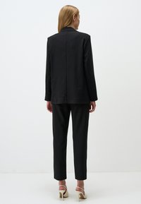 Completo nero a righe con giacca su misura e pantaloni slim-fit. Tessuto liscio, maniche lunghe e dettaglio con spacco posteriore. Scarpe con tacco alto.