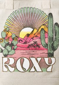 Borsa in tela con un design colorato di un tramonto che presenta montagne, cactus e palme, con la parola "ROXY" in caratteri grandi ben in vista.
