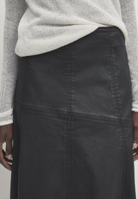 Gonna nera con una texture liscia e dettagli di cuciture visibili, abbinata a un top leggero a maniche lunghe in maglia di colore neutro.