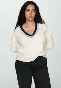 V-ringad tröja i krämfärg med kontrasterande svart och ljusblå kant. Har långa ärmar och en avslappnad passform. Bärs med svarta jeans.