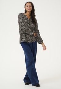 Blouse à manches longues dans un motif abstrait beige et marron, associée à un jean en denim bleu à jambes larges et des chaussures noires, offrant une coupe décontractée.