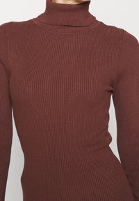 Top de cuello alto acanalado en color burdeos con mangas largas; presenta un diseño ajustado y una tela de punto texturizada.