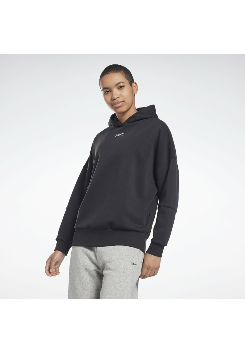 Schwarzer Kapuzenpullover mit geripptem Saum und Bündchen, ausgestattet mit einem kleinen weißen Logo auf der Brust, kombiniert mit grauen Sweatpants.